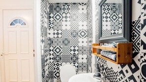 Ein Badezimmer mit Toilette, Waschbecken und Spiegel. Die Wände sind mit schwarz-weißen Fliesen verziert.
