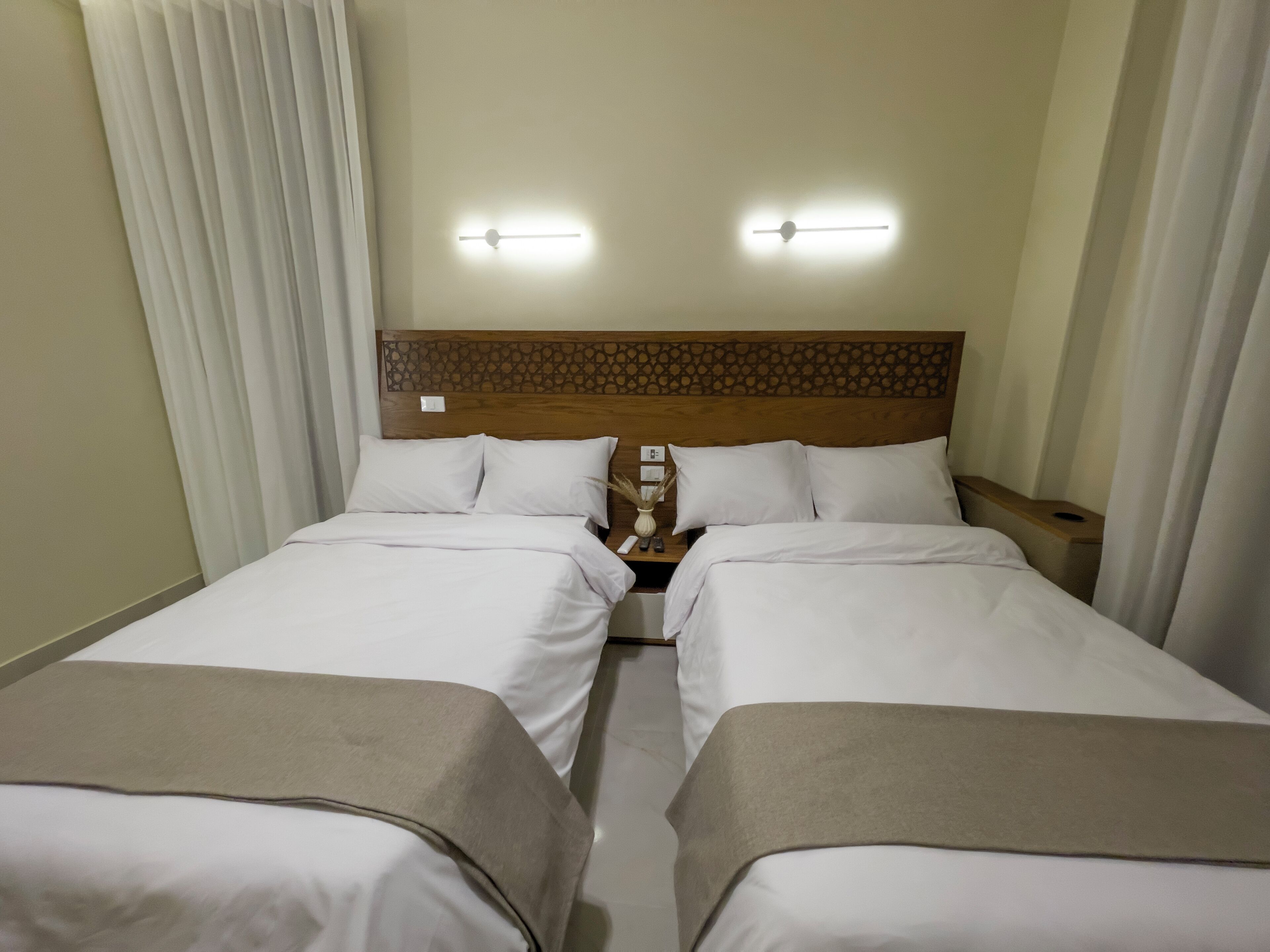Una habitación de hotel con dos camas individuales, un cabecero de madera, mesitas de noche y un buró con lámpara.