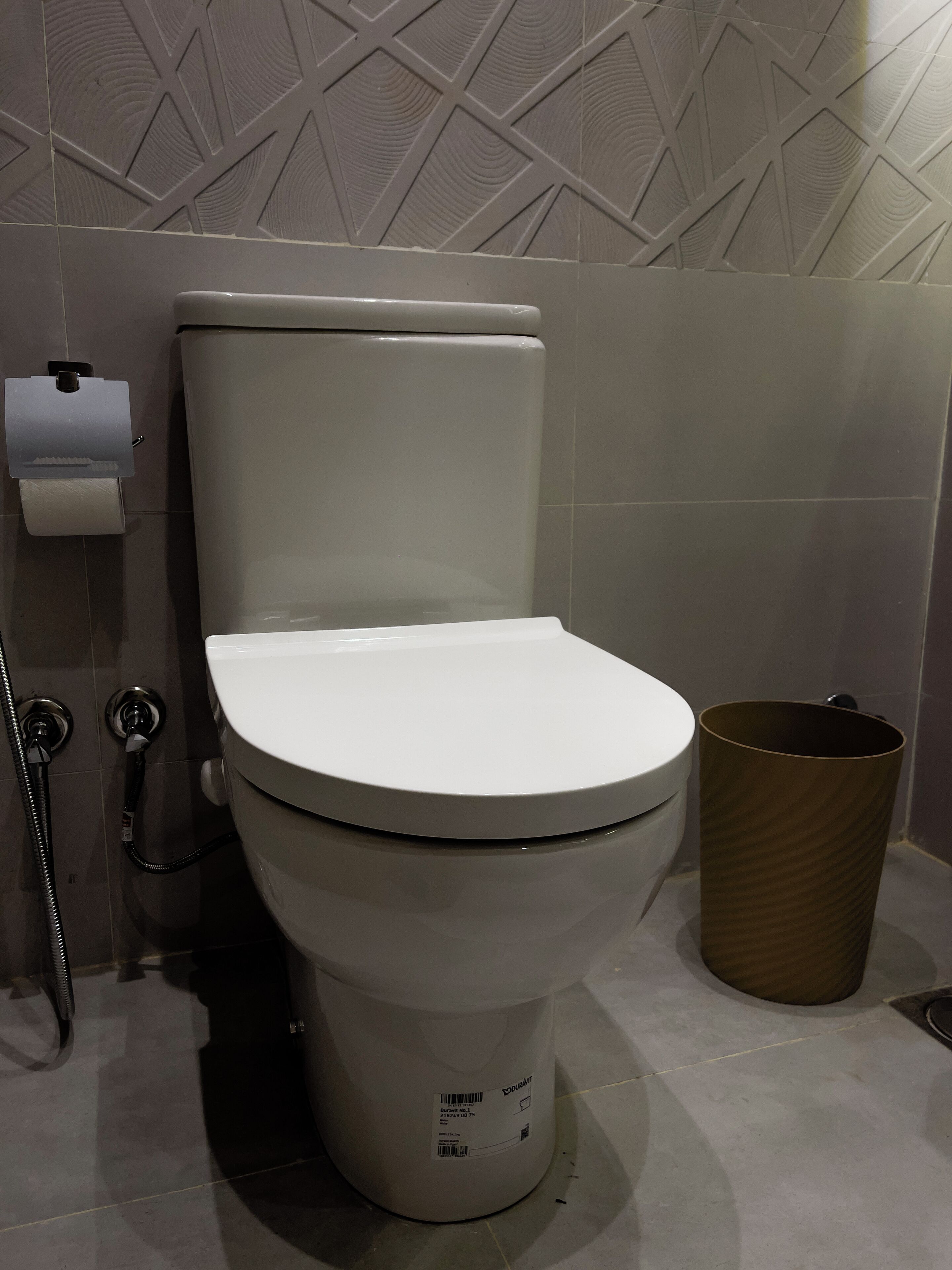Des toilettes avec un abattant blanc, un porte-serviettes en papier et une poubelle.