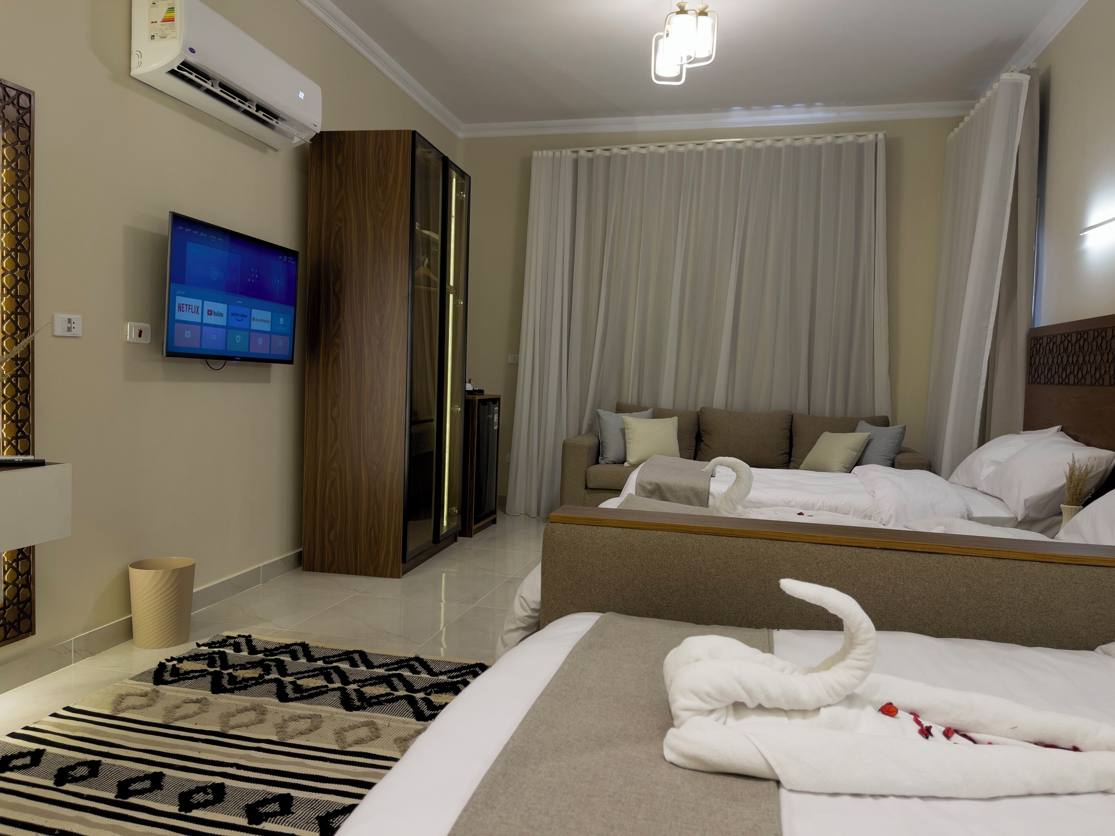 Habitación de hotel con una cama grande, una cama más pequeña, un televisor en la pared y un armario.