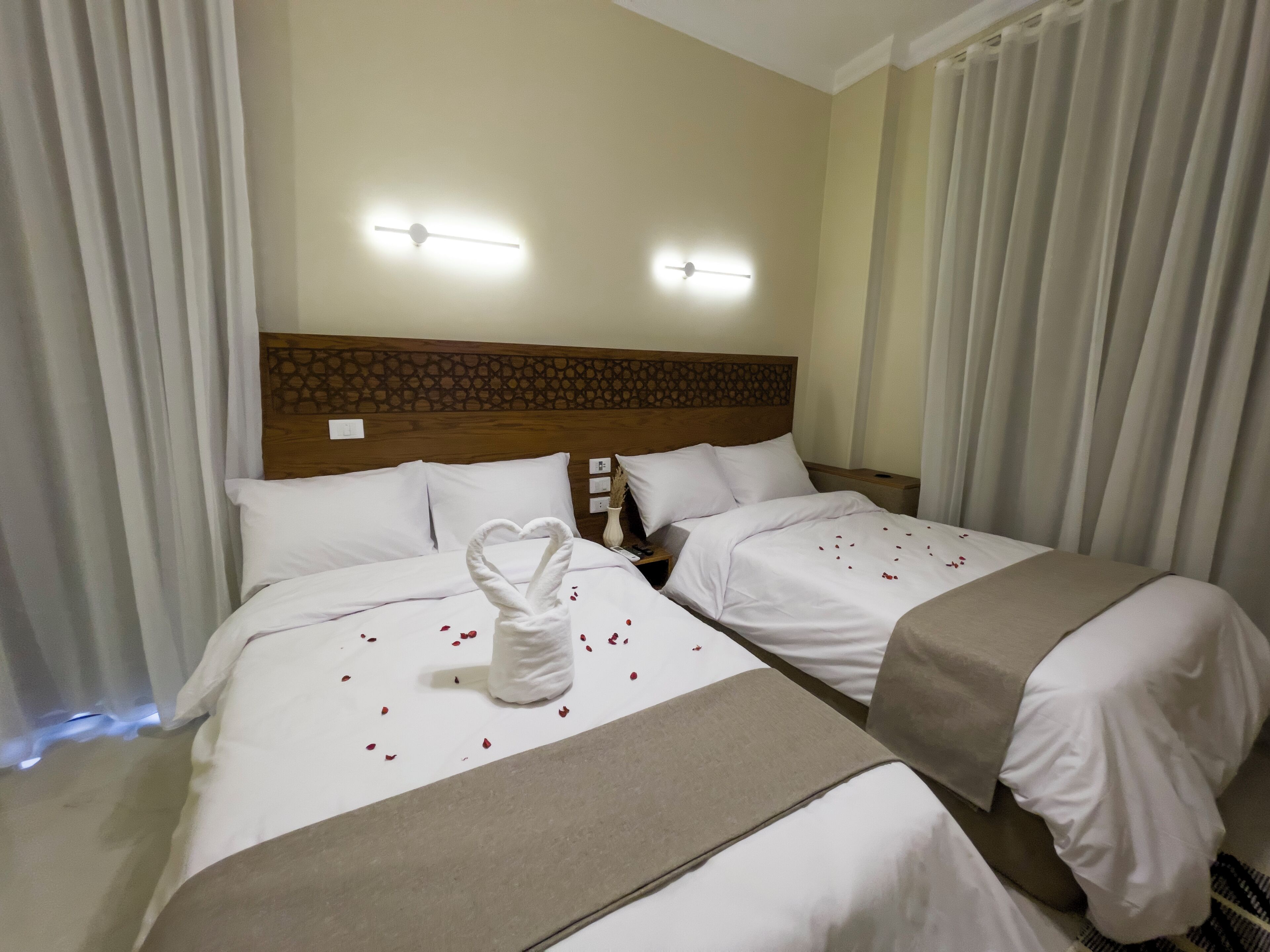 Een hotelkamer met twee bedden, een houten hoofdbord en een decoratieve handdoek op het bed.