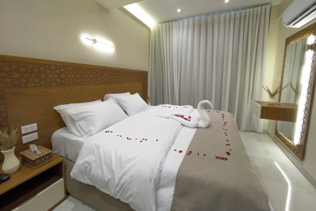 A hotel room with a neatly made bed, a bedside table with a tissue box, a mirror, and a ceiling light.