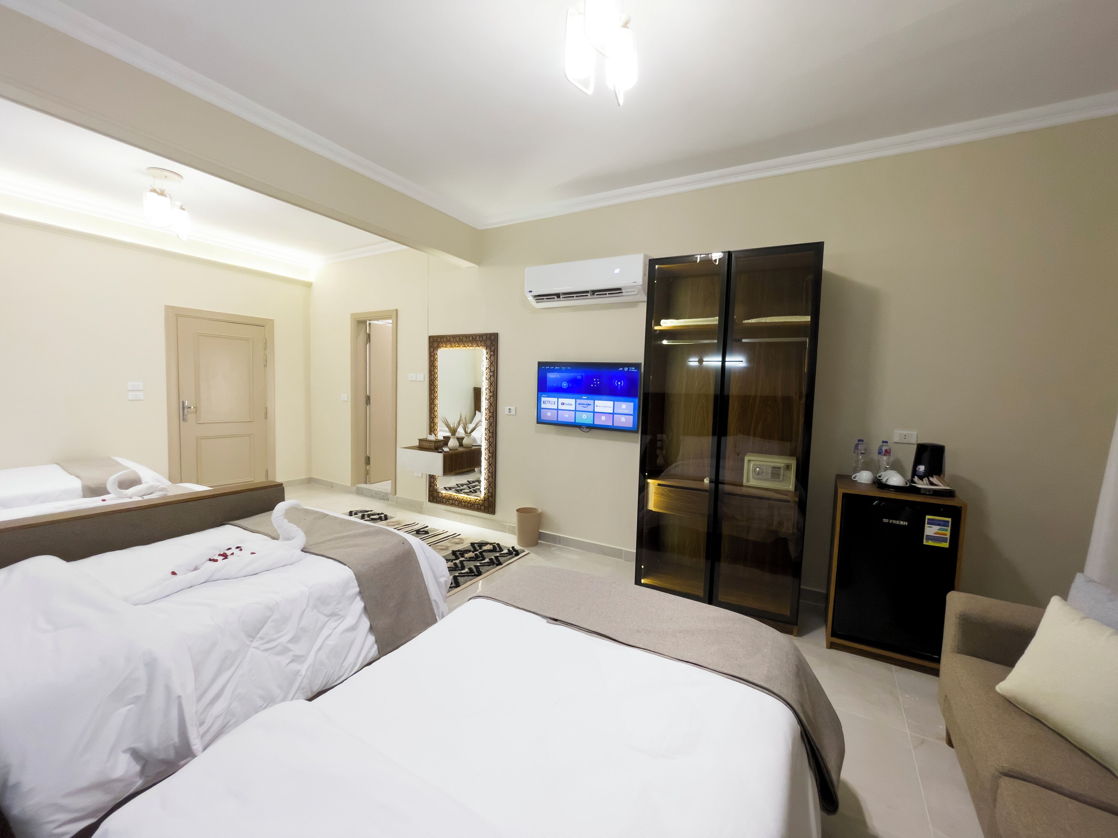 Een hotelkamer met twee bedden, een televisie, een minibar en een kledingkast.