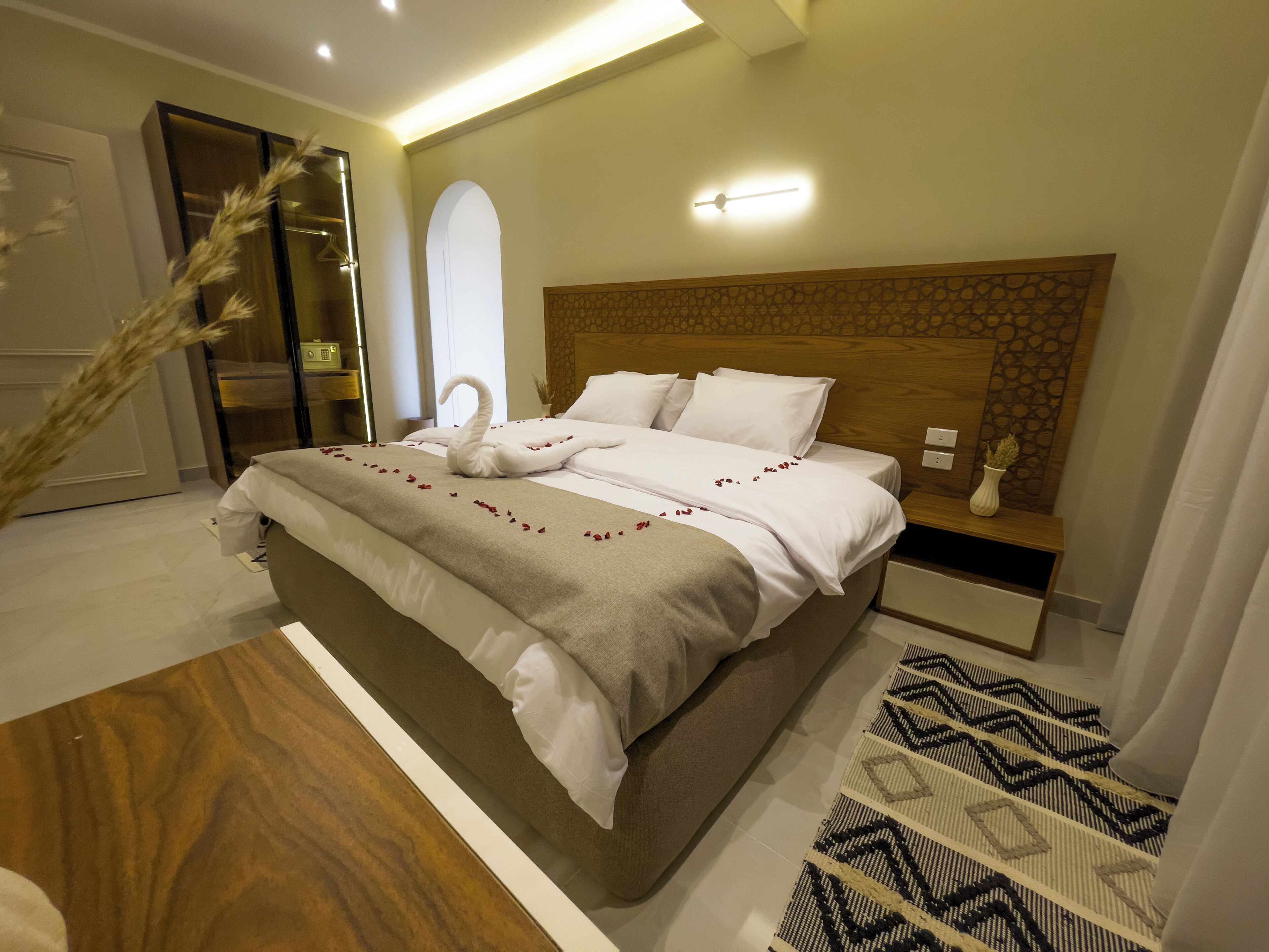 A modern hotel room with a large bed, a wooden headboard, and a decorative wall panel.