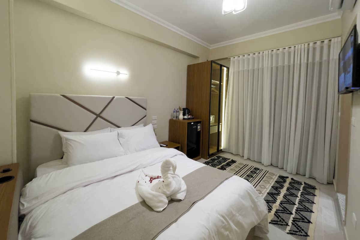 A hotel room with a large bed, a wooden wardrobe, a desk with a lamp, and a TV on the wall.