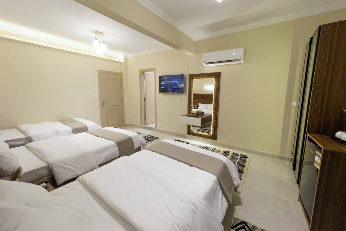 A hotel room with three beds, a TV, an air conditioner, and a wardrobe.