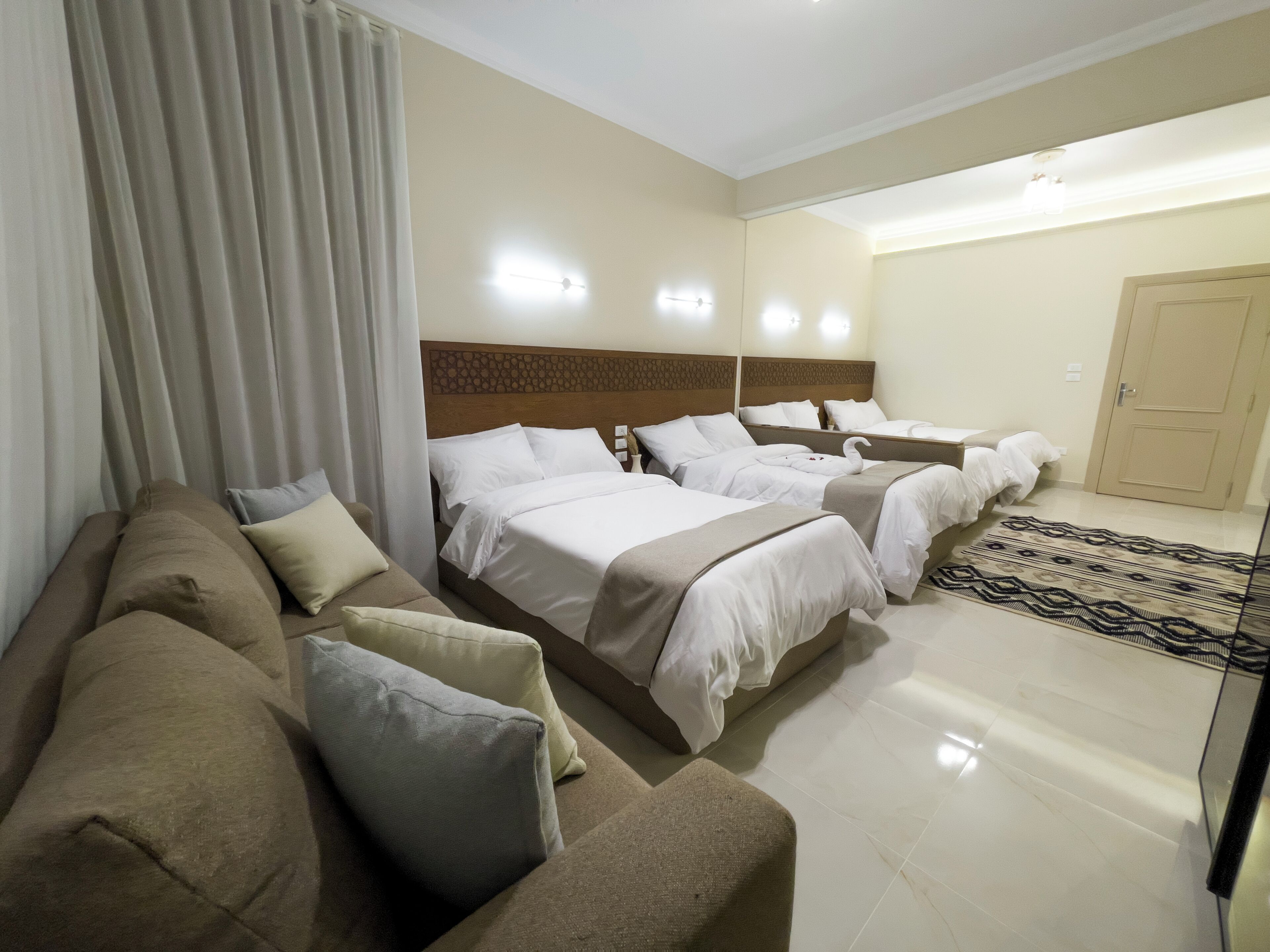 A hotel room with a sofa, two beds, a patterned rug, and a door.