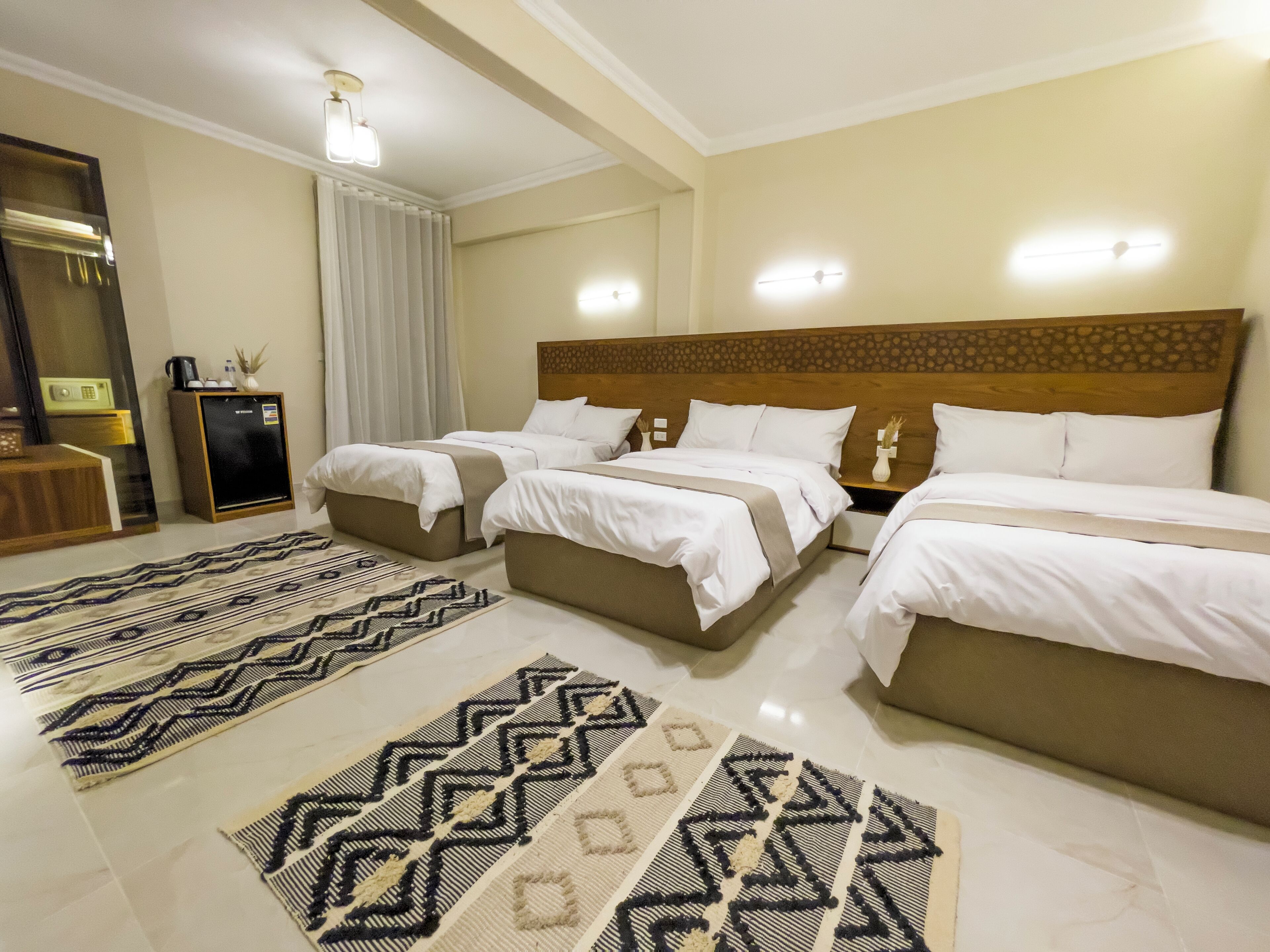 A hotel room with three beds, a minibar, a desk, and a patterned rug.