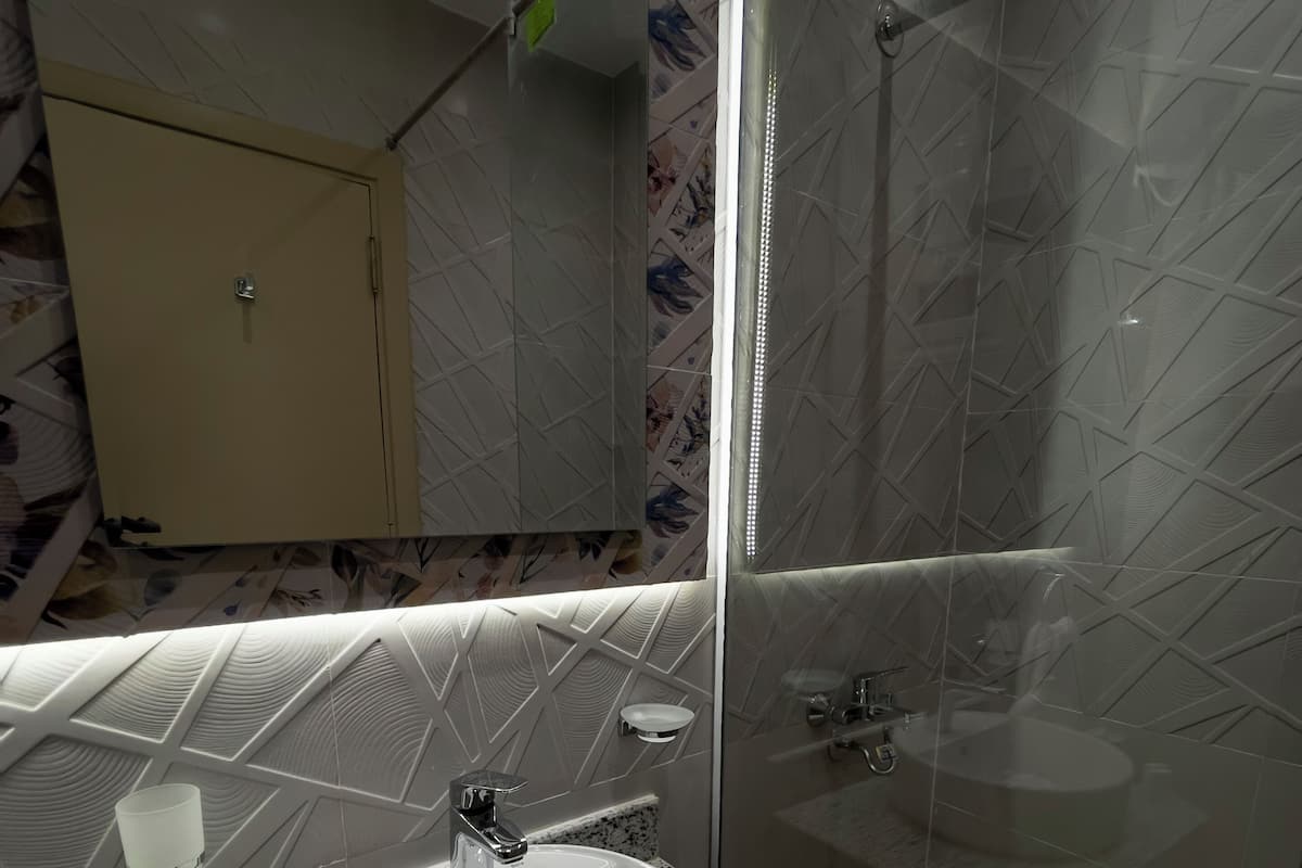 A modern bathroom with a white sink, a glass shower enclosure, and a vanity with a speckled countertop.