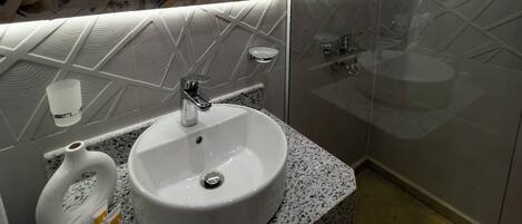 A modern bathroom with a white sink, a glass shower enclosure, and a vanity with a speckled countertop.