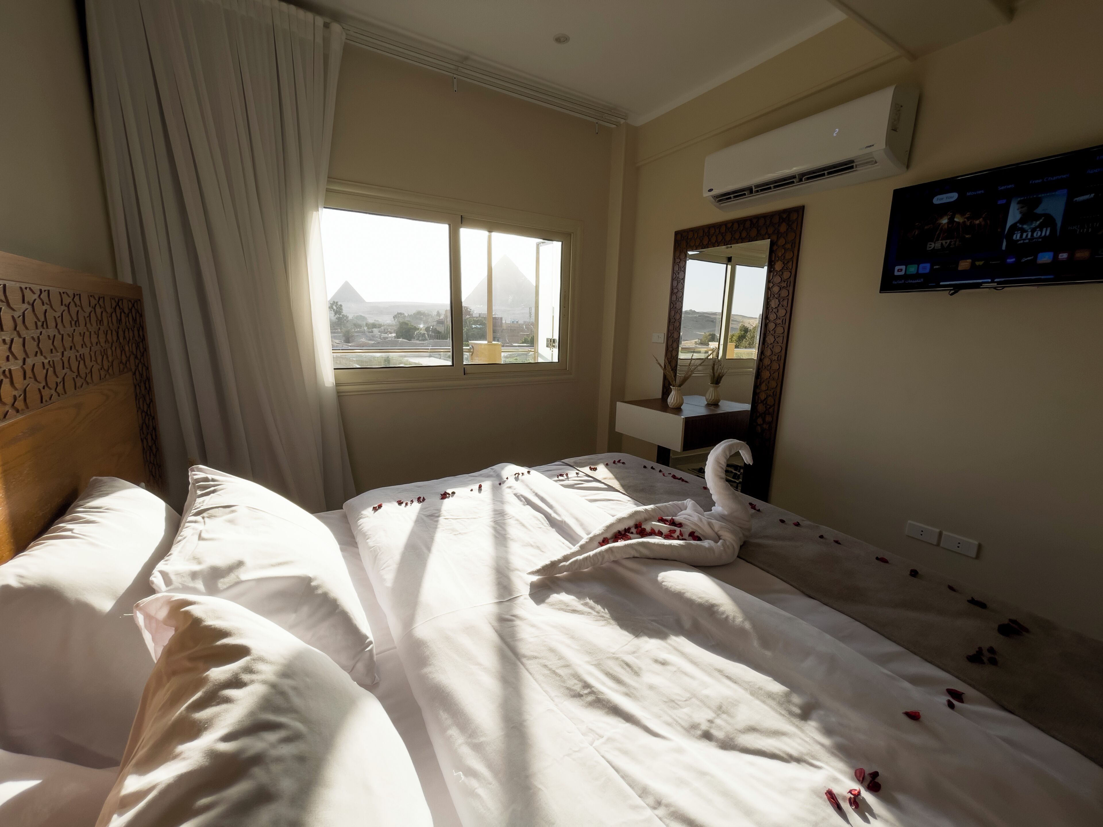 A hotel room with a bed, a window with a view of mountains, an air conditioning unit, and a television on the wall.