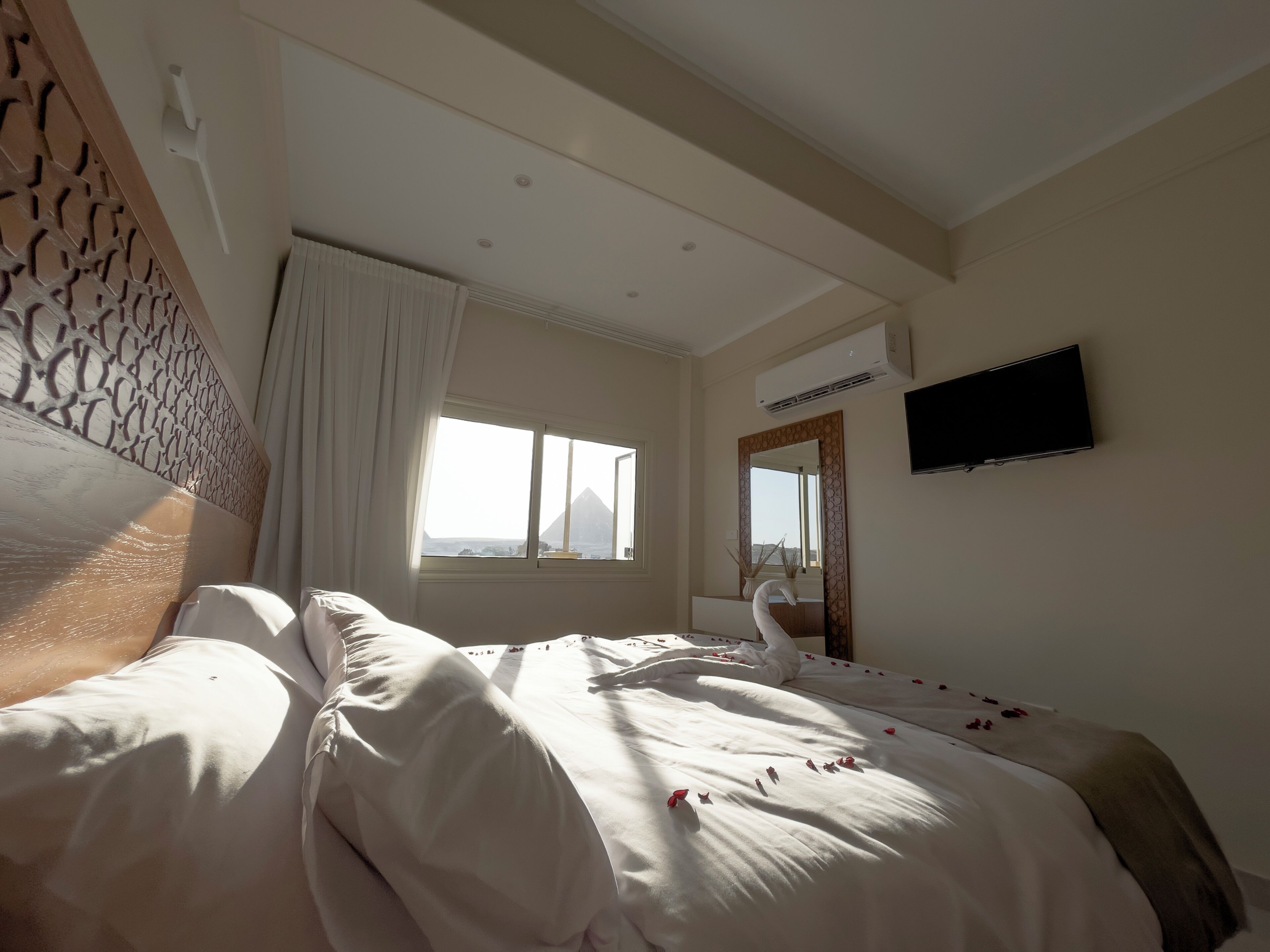 Une chambre d’hôtel équipée d’un lit, d’une fenêtre avec des rideaux, d’un climatiseur et d’un téléviseur à écran plat fixé au mur.