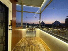 Un balcón con piso de madera, paredes de vidrio y vista a una montaña al atardecer.