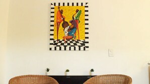 Dos sillas de mimbre con cojines, una consola negra con plantas en macetas y una obra de arte enmarcada en la pared.