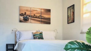 Una cama con una colcha blanca, una almohada verde y una planta verde grande a su lado.