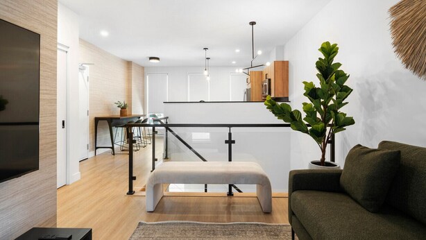 Una sala moderna con un sofá, un banco, un televisor y un comedor con sillas y una mesa.