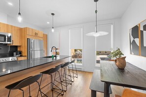 A modern kitchen with a central island, bar stools, a dining table, and a view of the outside. - Grand New 2bdr in Habitat Plateau by Denstays (Montréal)