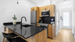 Una cocina moderna con encimera negra, armarios de madera, refrigerador de acero inoxidable, microondas y estufa.
