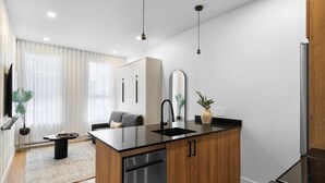Cocina moderna con lavavajillas, armarios de madera, encimera negra e iluminación colgante.