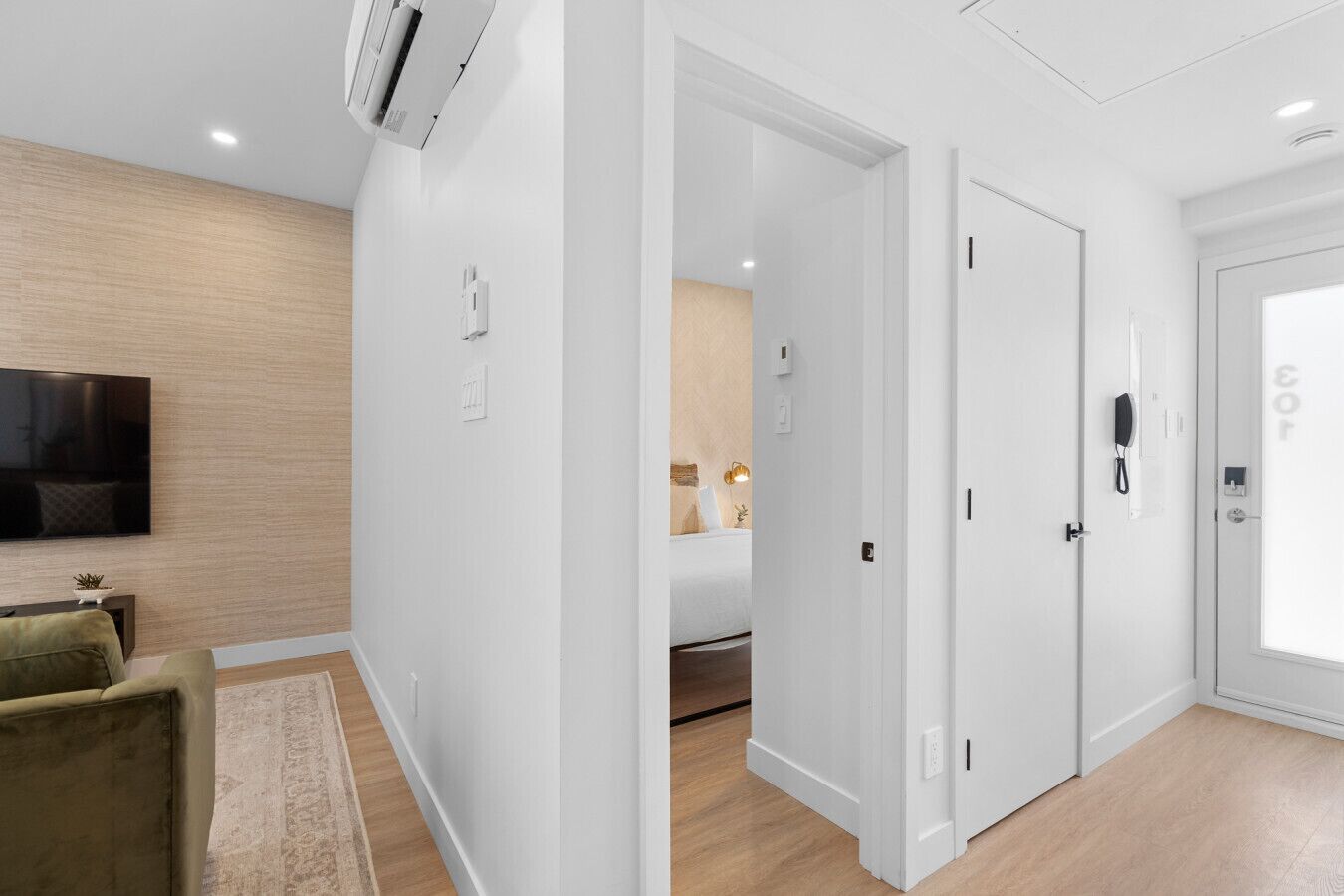 A modern hotel room with a flat-screen TV, a sofa, a wooden floor, and a door with a phone.