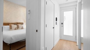 Ein Hotelzimmer mit Bett, einer weißen Tür und einem Flur mit hellem Boden.