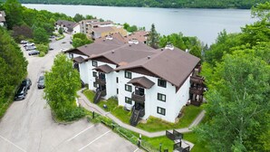 A multi-story hotel with a central courtyard, surrounded by lush greenery and a lake view. - Stunning One-Bedroom Condo With Lake View (Mont-Tremblant)