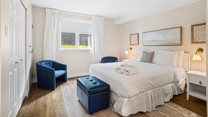 A hotel bedroom with a large bed, a blue chair, a nightstand with a lamp, and a window with curtains. - Stunning One-Bedroom Condo With Lake View (Mont-Tremblant)
