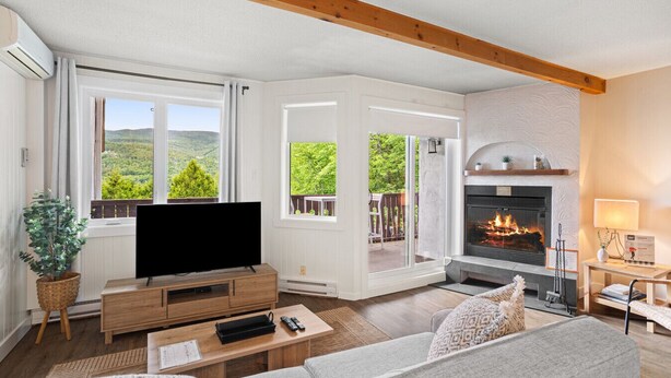A living room with a fireplace, large windows, and a flat-screen TV. - Stunning One-Bedroom Condo With Lake View (Mont-Tremblant)