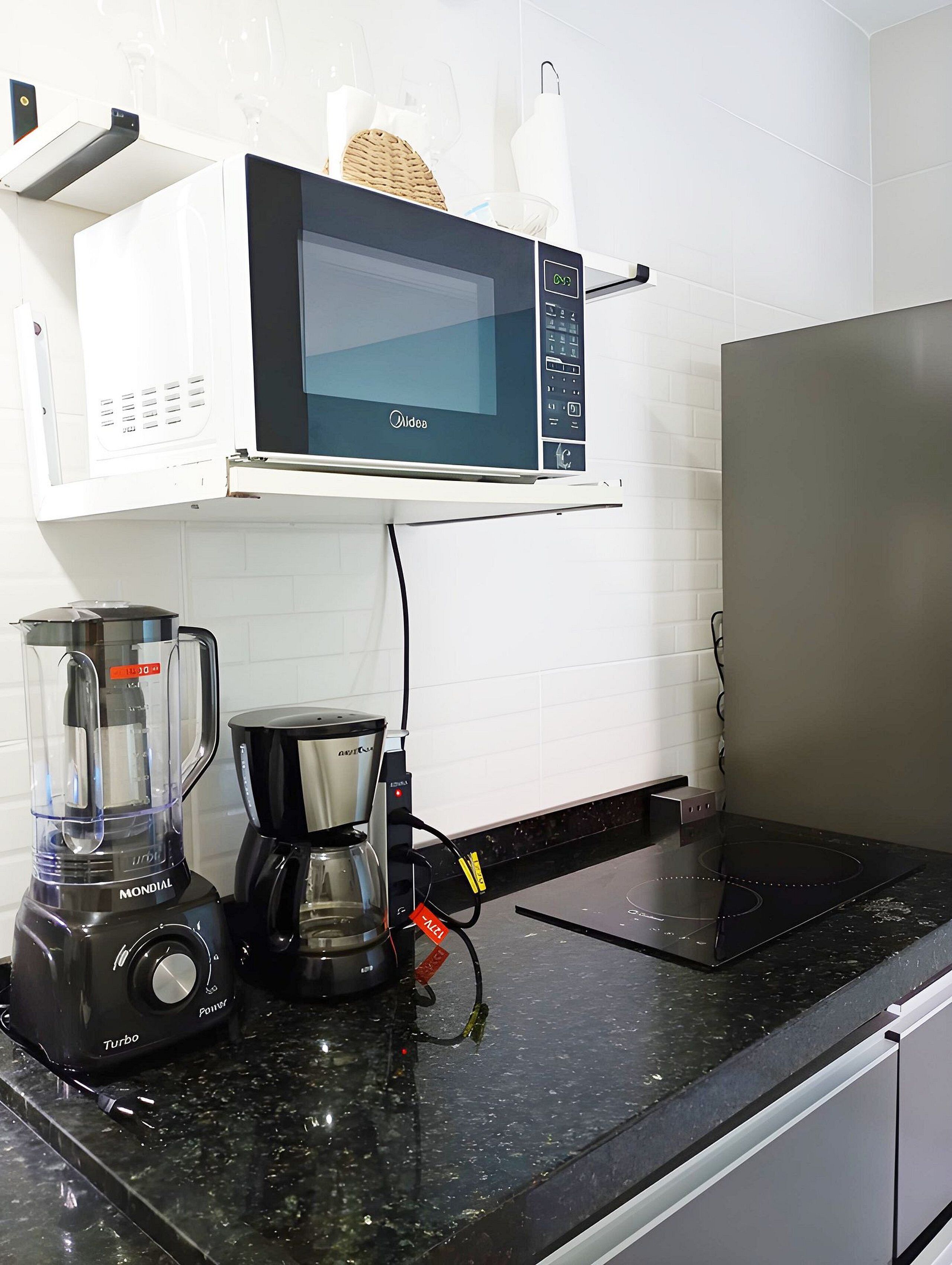 Una cocina con microondas, licuadora y cafetera sobre una encimera negra.