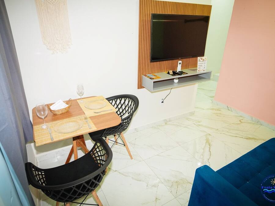 A dining area with a table set for two, a TV mounted on the wall, and a blue sofa in the background.