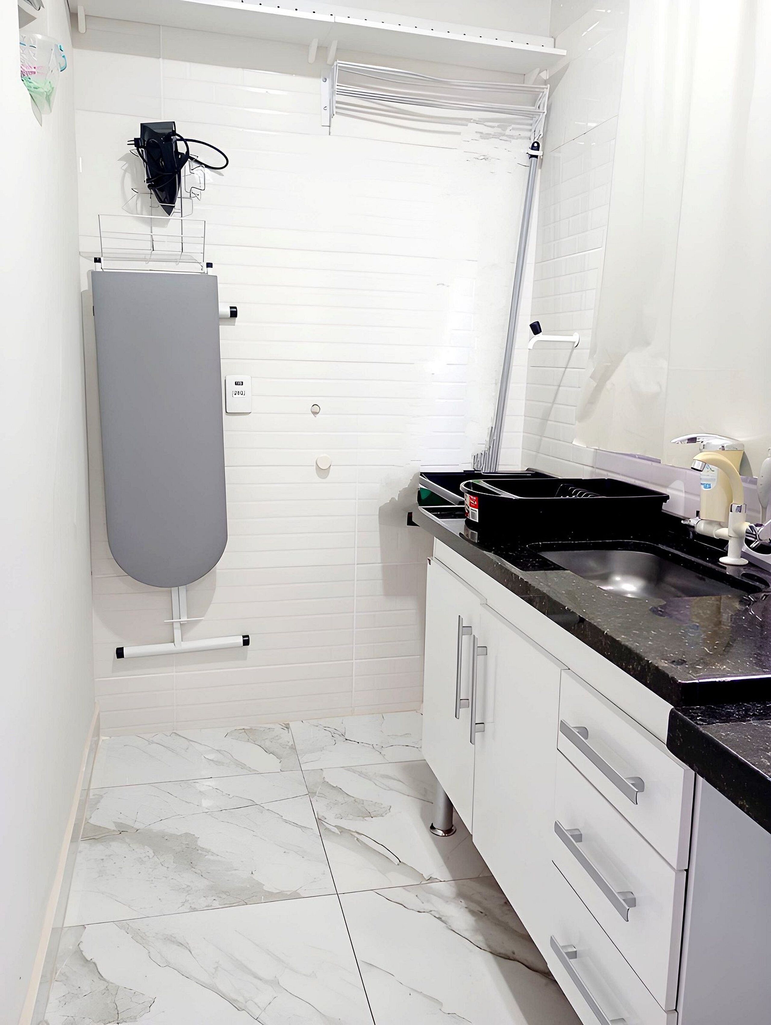 A bathroom with white tiled walls, a marble floor, a grey toilet, a black sink, and a white cabinet with drawers.