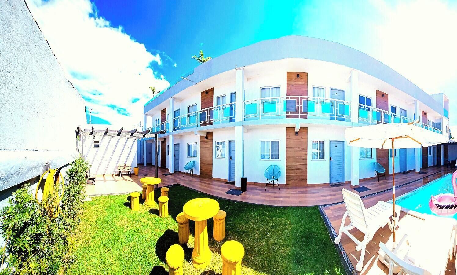 Un hotel de varios pisos con piscina, mobiliario exterior y un césped bien cuidado.