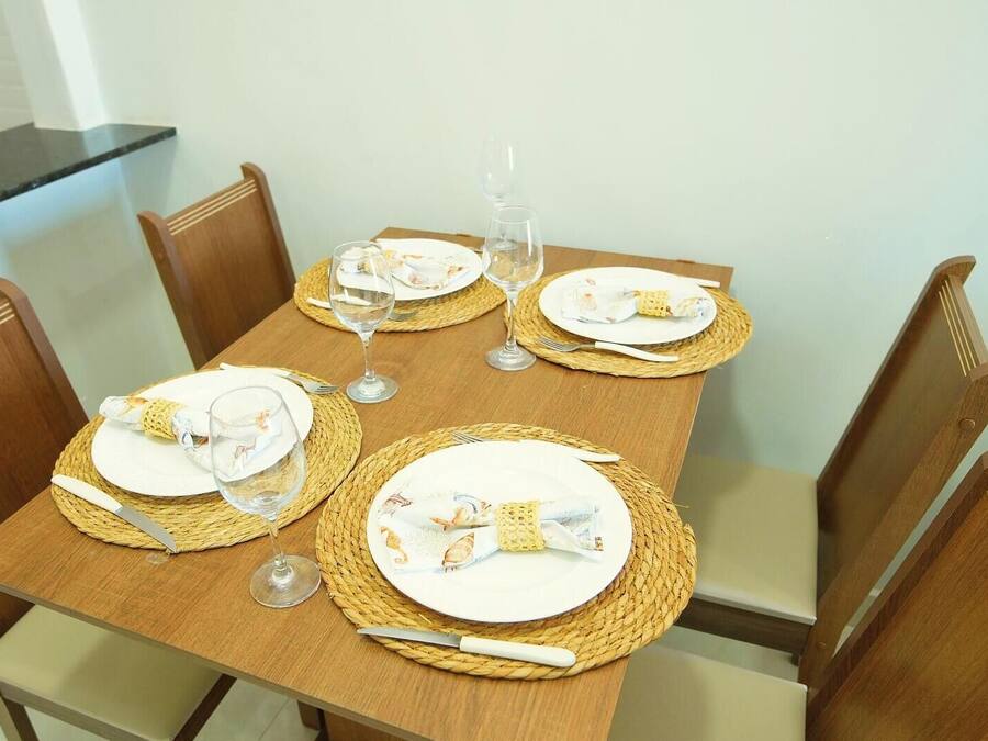 Una mesa de comedor preparada para cuatro personas, con individuales, platos, cubiertos y copas de vino.