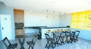 A modern kitchen area with a built-in stove, a sink, and a countertop. There are multiple tables and chairs arranged for dining. - Praia Studios (Vila Velha)