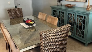 A dining area with a glass-top table, wicker chairs, a teal cabinet, and a map on the wall. - 2-bedroom 2 bathroom condo right on the beach in beautiful Naples, FL (Naples)