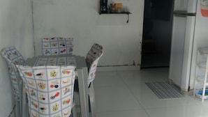 Un comedor con una mesa y sillas, un refrigerador y una repisa con utensilios de cocina.