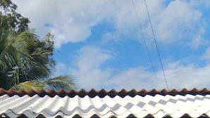 Un edificio pequeño de una sola planta con techo de metal corrugado y fachada azul claro. Tiene una puerta metálica con un ventanal arriba, y un buzón pequeño adosado a la pared.