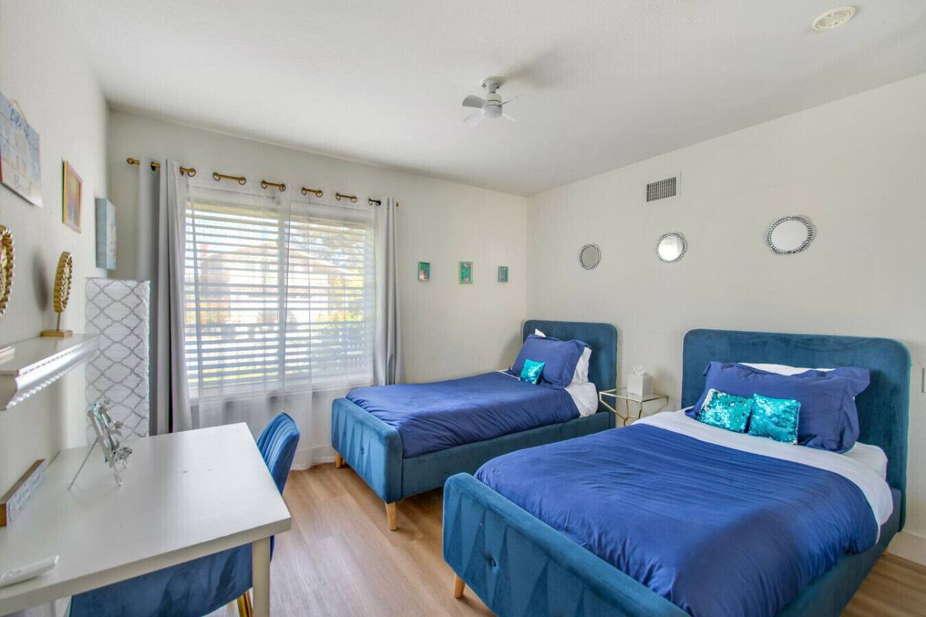A bedroom with two beds, a desk, and a window with blinds.