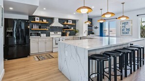 Une cuisine moderne dotée d’un grand îlot central, de tabourets de bar et de luminaires suspendus.