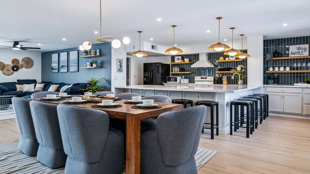 Une cuisine moderne dotée d’un îlot central, de luminaires suspendus et d’un coin repas avec des chaises à revêtement gris.