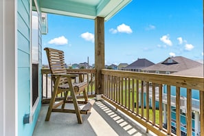 A wooden deck with a wooden chair, a railing, and a view of houses in the background.