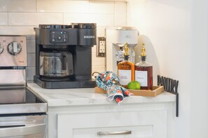A kitchen with a coffee maker, a kettle, and two bottles of syrup.