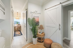 A hallway with a dining area, a large potted plant, a lamp, and a door with a sliding mechanism.