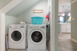 A laundry area with two front-loading washing machines, a teal laundry basket, and a wall-mounted drying rack.