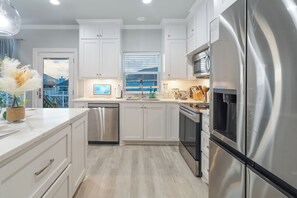 A modern kitchen with white cabinetry, stainless steel appliances, and a view of a pool through the window.