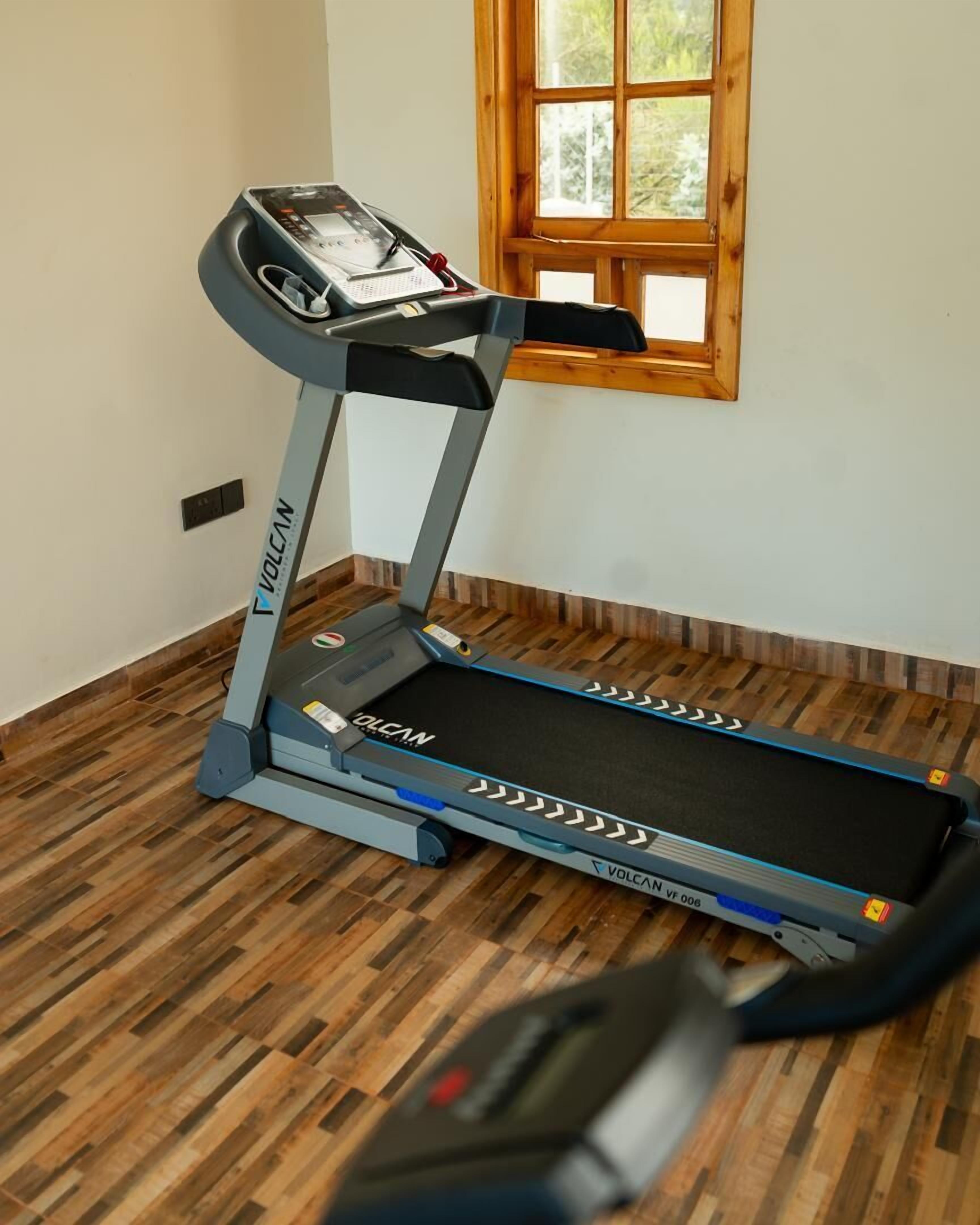 Una cinta de correr en una habitación con suelo de madera y una ventana con vista a árboles.