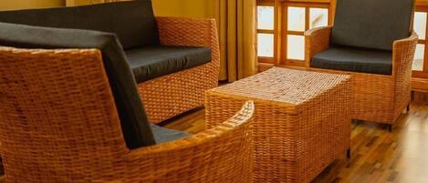A room with wicker furniture, including a sofa and armchairs, and a wooden floor.
