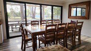 A dining area with a large wooden table and chairs, a fluffy rug, and a sliding glass door leading to an outdoor patio.