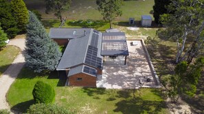 Ein Haus mit geneigtem Dach, Solaranlagen, einer überdachten Terrasse und einem eingezäunten Garten.