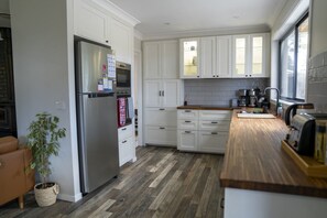 A modern kitchen with white cabinetry, a stainless steel refrigerator, and a wooden countertop. - Fettlers Lodge - zigzag railway, peaceful, acreage, pet friendly (Clarence)